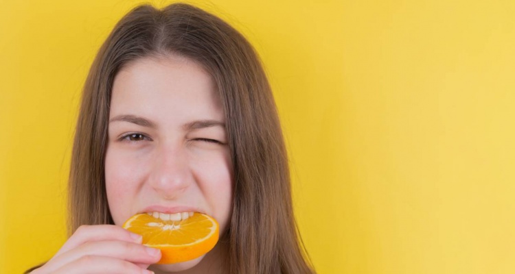 mujer mordiendo una naranja para la ระงับกลิ่นปาก