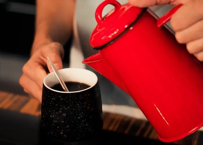 Una mujer echa café en una taza con una cafetera de color rojo