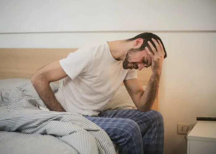 Un hombre sentadoen una cama con dolor de cabeza y mareos