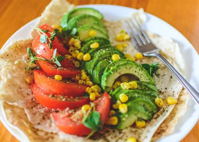 En tallerken vegansk mad med tomat, majs og avocado