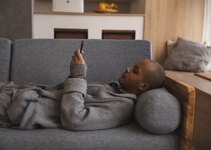 Um hombre tumbado no sofá com o móvel com sedentarismo